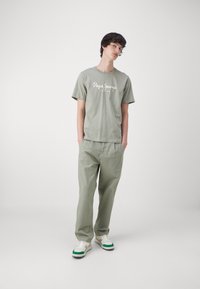 Camiseta de algodón verde claro con el logo de "Pepe Jeans London", combinada con pantalones de algodón a juego. Zapatillas blancas con acentos verdes completan el look.