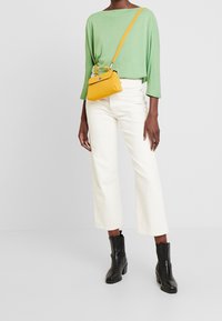 Groene gebreide trui, witte wijde jeans en zwarte enkelhoge laarzen. Gele crossbody tas met een sluiting en accentdetails.