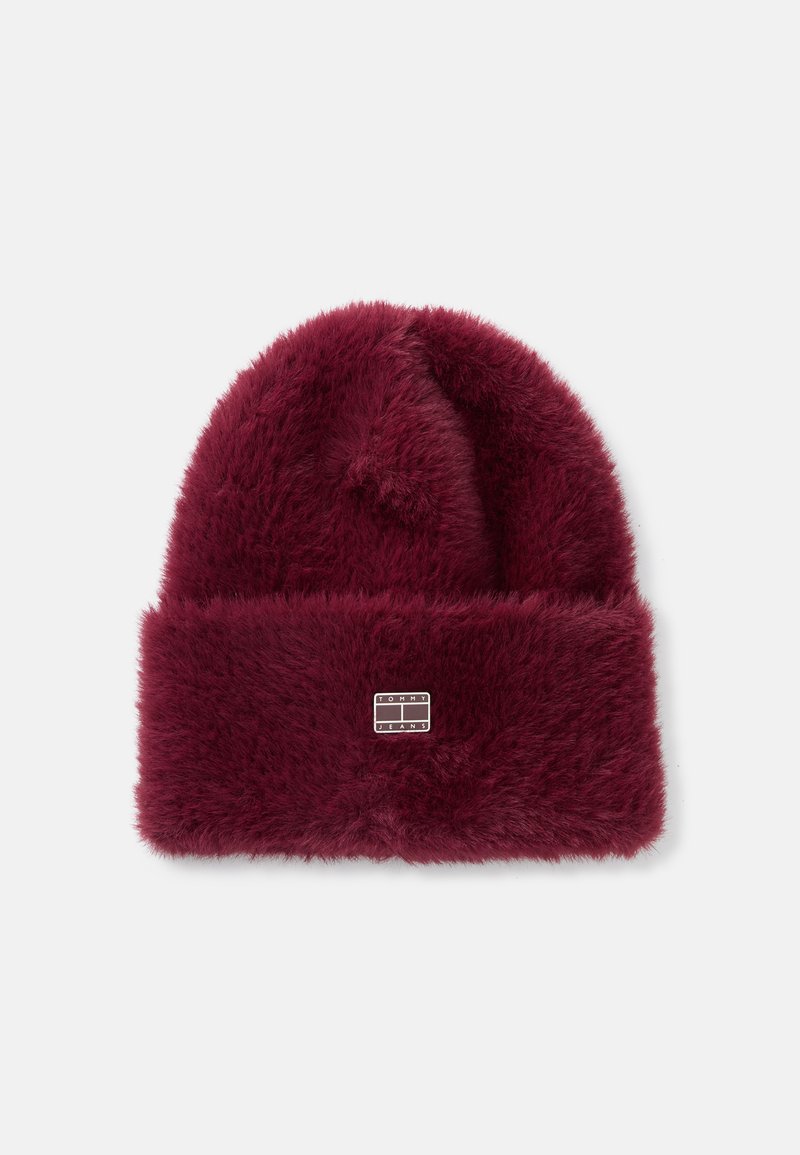 Caciulă burgundy cu o textură moale, asemănătoare blănii, și un tiv îndoit. Prezintă un mic tag argintiu cu brandul în față.
