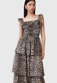 Abito maxi in stampa leopardata con strati di rouches, corpetto arricciato e spalline scese. La palette di colori include tonalità di beige e nero.