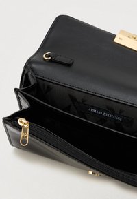 Μαύρη σύνθετη δερμάτινη τσάντα clutch με χρυσά αξεσουάρ; το εσωτερικό διαθέτει πολλαπλές θήκες και ετικέτα Armani Exchange. Ορατή κλειδαριά με φερμουάρ.