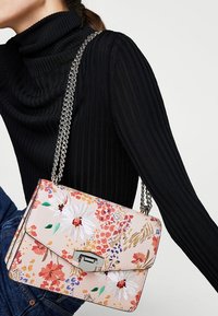 Sac à main à motif floral avec une surface texturée rose, une chaîne en argent et une fermeture à clasp de design rectangulaire.