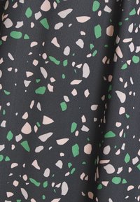 Tejido con un fondo negro que presenta un patrón de terrazo en rosa, verde y blanco, mostrando elementos texturizados de forma irregular.