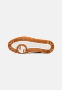 Semelle de chaussure avec bande de roulement en caoutchouc marron, semelle intermédiaire blanche, section circulaire transparente près du talon et texte "FILLING PIECES" embossé sur la semelle.