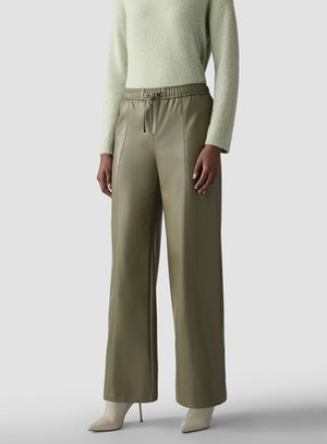 Person wearing olive green wide-leg faux leather pants with drawstring waist and beige pointed high-heeled boots, standing.