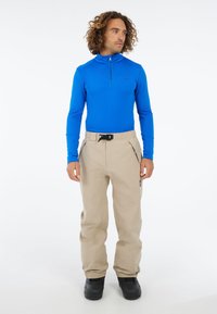 Blauw lange mouwen top met kwartrits, gecombineerd met beige waterdichte broek en zwarte laarzen. De outfit bevat verstelbare taillebanddetails.