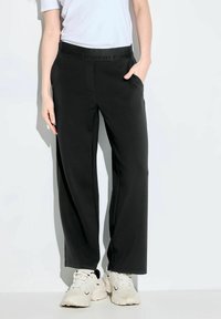 Černé kalhoty širokého střihu s elastickým pasem, na kterém je reliéfní vzor "POSITIVITA". Materiál vypadá hladce a má pružné vlastnosti.