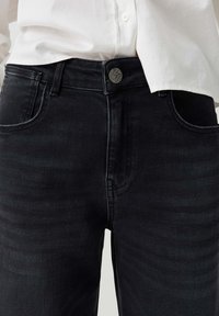 Black denim jeans with front pockets and belt loops worn with a white buttoned shirt tucked in at the waist.