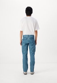 Pantalones cargo de denim azul claro con múltiples bolsillos, pierna recta y un corte relajado. Combinados con una camiseta blanca básica.