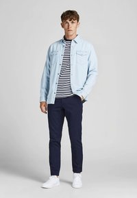 Chemise en denim bleu clair, t-shirt rayé bleu marine et blanc en dessous, pantalon bleu marine foncé et baskets blanches. Design simple, coupe décontractée.
