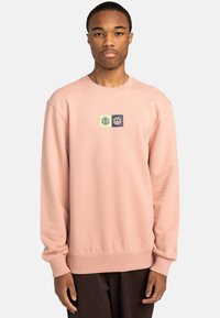 Light pink sweatshirt with ribbed cuffs, round neckline, and a central logo in green and navy on a block background. Soft texture, casual design.