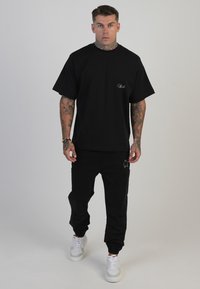 Černé bavlněné tričko s krátkými rukávy a malým logem na hrudi, spojené s černými tepláky a bílými teniskami.