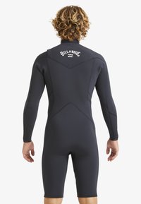 Traje de neopreno negro con mangas largas, hecho de material elástico. Presenta costuras planas y un logo en la parte superior de la espalda. Diseño ajustado al cuerpo.