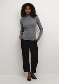 Grauer langärmeliger Rollkragenpullover kombiniert mit schwarzen, weit geschnittenen Hosen und schwarzen Ballerinas. Glatter Stoff mit einer figurbetonten Silhouette.