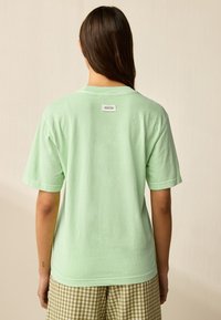 Ljusgrön bomulls-t-shirt med korta ärmar, avslappnad passform och en liten etikett i bakre nacken. Bärs med rutiga shorts.