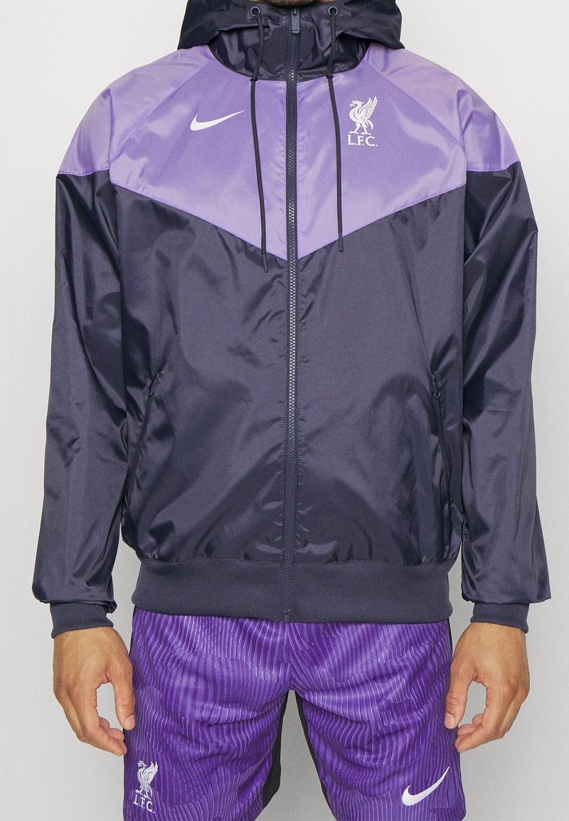 Navy and purple Nike jacket with hood, zip, and L.F.C. logo, paired with purple striped shorts. Made of glossy, lightweight material.