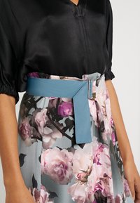 Květinové šaty s saténovým černým topem, šedou sukní s růžovými květinovými vzory a texturovaným modrým páskem s kovovou sponou.