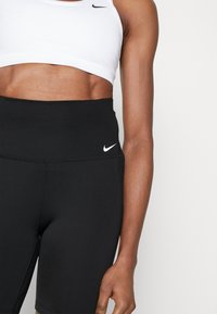 Leggings noirs taille haute avec un logo Nike discret, associés à un soutien-gorge de sport court blanc, présentant un design simple et moderne.