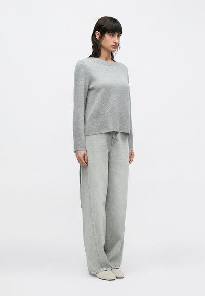Ανοιχτό γκρι πουλόβερ με άνετη εφαρμογή, στρογγυλή λαιμόκοψη και μακριά μανίκια, συνδυασμένο με ανοιχτό γκρι τζιν παντελόνι φαρδιάς γραμμής. Λεία υφή, μίνιμαλ σχεδιασμός.