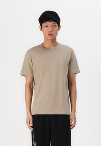 T-shirt beige in cotone a maniche corte con scollatura rotonda e un piccolo logo ricamato sul petto sinistro. Tessuto liscio, vestibilità casual.