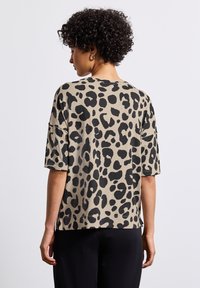 Leopard print t-shirt in beige with black spots. Short sleeves, relaxed fit, round neckline, soft texture, and stitched hem details.