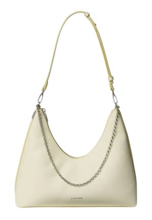Kleine crèmekleurige leren handtas met een korte riem en een decoratieve zilveren ketting aan de voorkant, Calvin Klein-logo zichtbaar bij de onderkant.