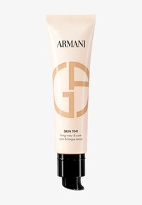 Tubo di Armani Skin Tint con corpo beige morbido, pompa nera e grande logo beige. Il testo include "long-wear & care". Texture liscia.