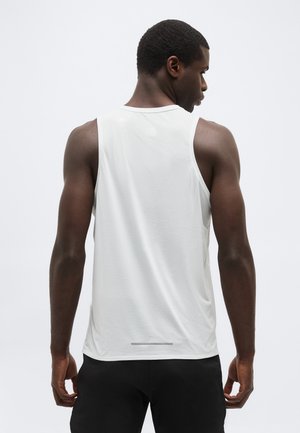 Mann sett bakfra, iført en hvit ermeløs treningsskjorte og svarte shorts, mot en enkel lys bakgrunn.