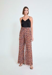 Camisola de satén negro con tirantes ajustables, combinada con pantalones de pierna ancha con estampado de leopardo en tonos naranja, negro y azul.