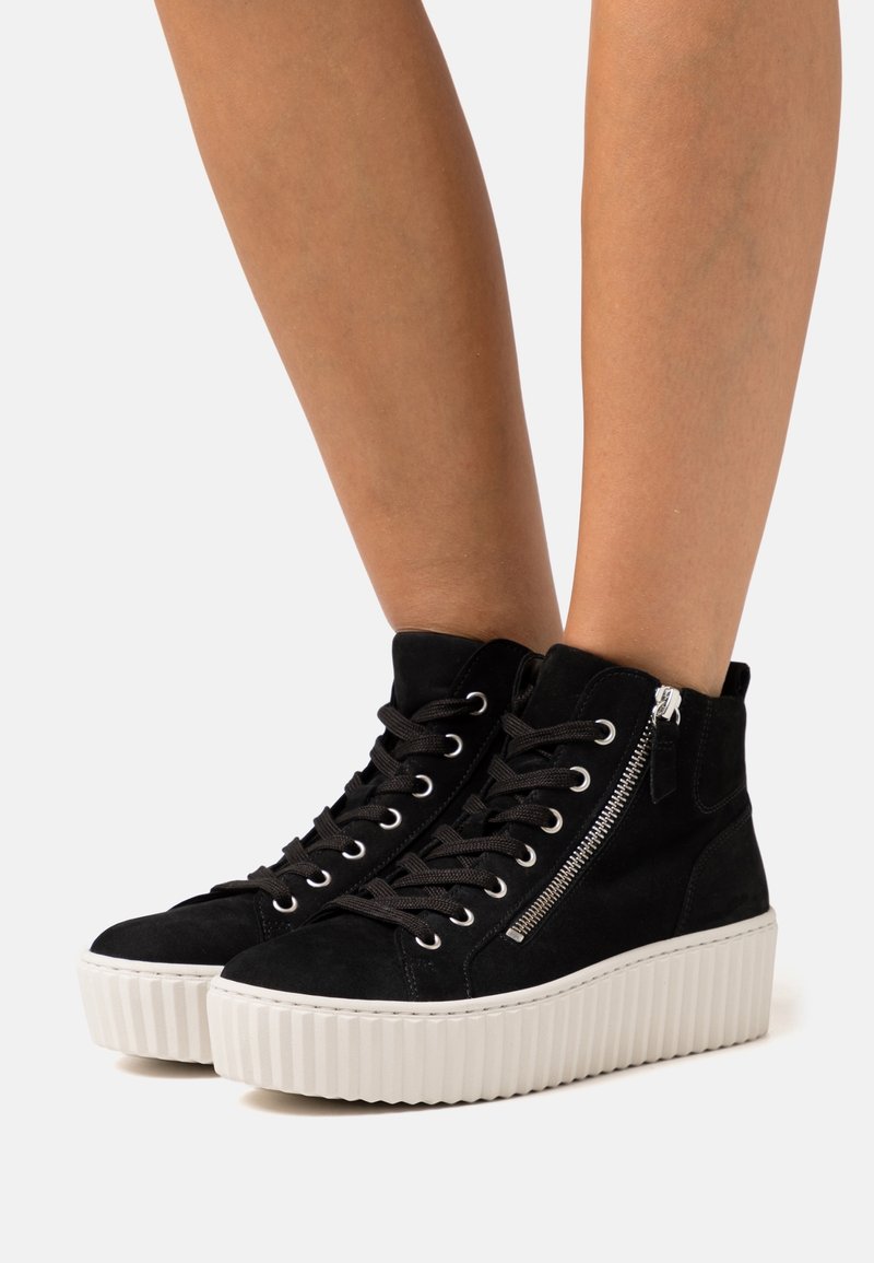 Mustat mokkanahkaiset korkeakärkiset tennarit, joissa on valkoinen platform-pohja, etulankat ja sivuvetoketju.