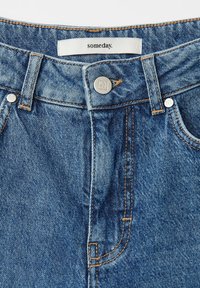 Denim jeans in a medium blue shade featuring a button closure, contrast stitching, and a label that reads "someday." Classic five-pocket design.