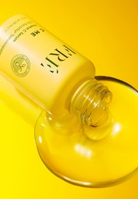 Siero alla vitamina C in una bottiglia di vetro giallo opaco con un tappo di plastica, rovesciato per rivelare un liquido giallo lucido che si accumula sotto.