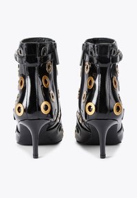Czarne lakierowane botki do kostek na szpilce. Posiadają złote oczka i zamek błyskawiczny po boku. Gładka tekstura i dopasowany krój.