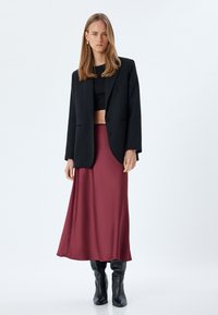Blazer oversize nero, top corto nero, gonna midi fluida bordeaux e stivali neri al ginocchio. Tessuto morbido, design minimalista.