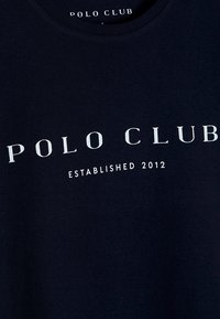 Námorně modré bavlněné tričko s bílým nápisem: "POLO CLUB" a "ZALOŽENO 2012" na přední straně. Klasický design s kulatým výstřihem.