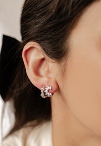 Pendientes plateados en forma de flor con piedras preciosas transparentes, que presentan diferentes tamaños y ángulos, dispuestos en un diseño circular.