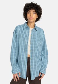 Lichtblauw geruite shirt gemaakt van zacht materiaal, met een knoopsluiting aan de voorkant, lange mouwen en een borstzak.