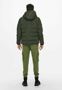 Green padded jacket with a hood, featuring quilted sections, paired with matching green cargo pants. Black footwear completes the outfit.