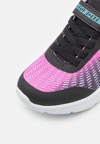 Zapatilla deportiva negra y rosa con parte superior de malla, acentos morados en contraste, suela texturizada y cordones negros. Presenta el logotipo en la correa.