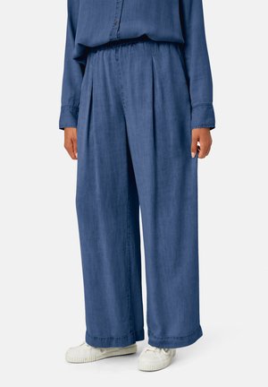 Pantalon large, bleu marine, en tissu doux avec une taille élastique et des plis. Associé à des baskets blanches.