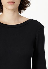 Must räägitud must pikkade varrukatega topp, millel on lai ümar kaelus ja õmbluse detail. Sile tekstuur, kitsas vorm ja minimalistik disain.