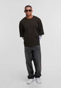 Sort oversized t-shirt med korte ærmer, parret med mørkegrå jeans og hvide sneakers. Solbriller fuldender det afslappede look.