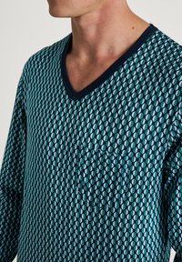 Blauwe en groene geometrische patroon met een V-hals en lange mouwen. Contrast navy ribgebreide halslijn en zak aan de linkerkant. Zachte stofstructuur.