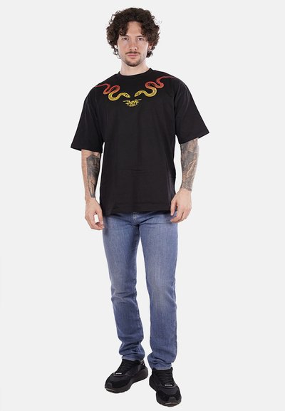 T-shirt nera in cotone con grafica di serpente rossa e gialla e vestibilità ampia. Abbinata a jeans azzurri e sneakers nere.