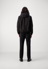 Zwarte bomberjack met capuchon, voorzien van een eenvoudig ontwerp, elastische manchetten en een slanke pasvorm, gecombineerd met rechte zwarte broek en laarzen.