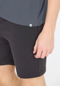 Grå t-shirt med korta ärmar, tillverkad av mjukt tyg, ihop med svarta shorts som har en slät yta och en nära passform.