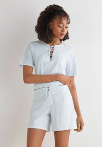 Lichtblauw gestreepte top met vetersluiting bij de hals, gecombineerd met een bijpassende short met een trekkoord in de taille. Beide hebben een zachte, casual stof.