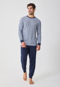 Chemise grise à manches longues avec col bleu marine, ornée d'un petit logo. Associée à un pantalon de détente bleu marine, tous deux confectionnés dans un tissu doux.