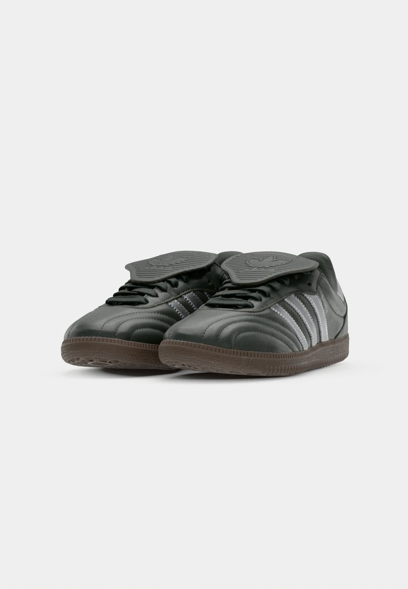 Chaussures de sport en cuir noir avec trois rayures argentées. Elles disposent d'une semelle texturée et d'une languette rembourrée avec un logo en relief. Design à embout rond.