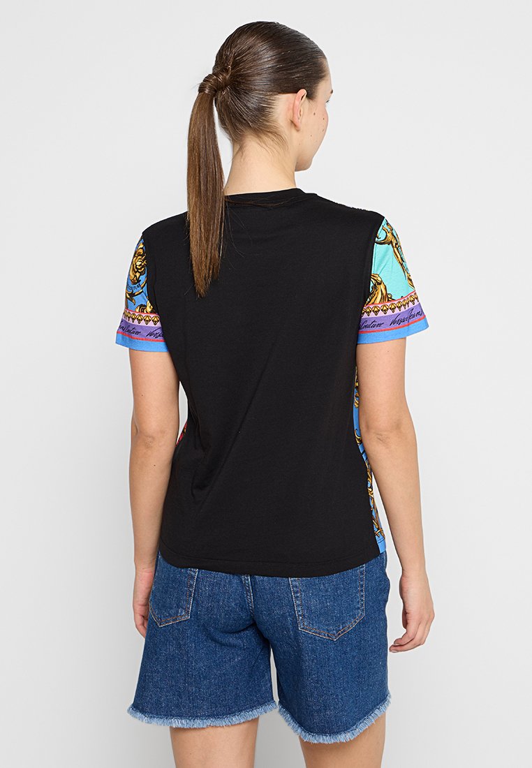 Czarna koszulka z krótkim, wzorzystym rękawem, zdobiona niebieskimi, żółtymi i fioletowymi akcentami; noszona z dżinsowymi szortami. Gładka faktura tkaniny.